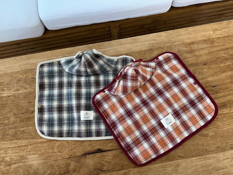 Two plaid cape dog vests in brown and orange checkered patterns by NKpup