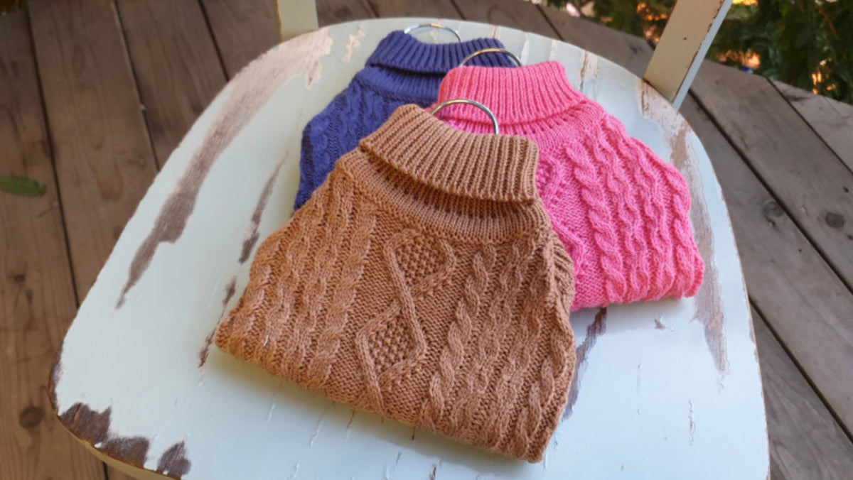 Three turtleneck cable knit dog vests in brown, pink, and navy blue.