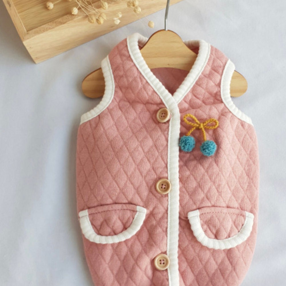 NKpup pink quilted dog vest with white trim, buttons, and blue cherry pom-pom detail