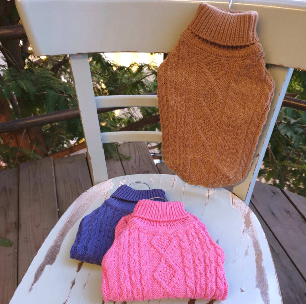 Three turtleneck cable knit dog vests in brown, navy, and pink.