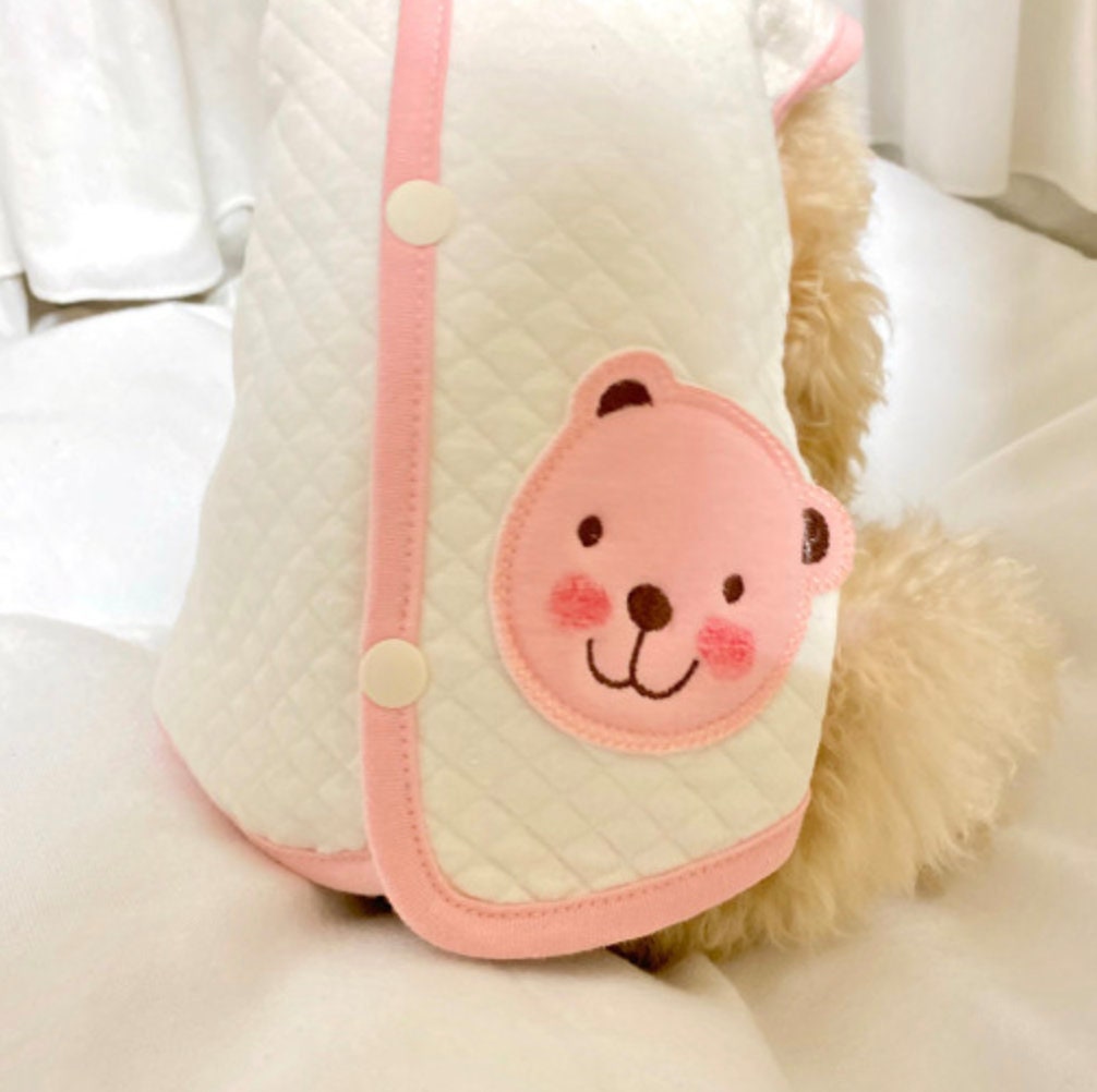 White quilted organic dog vest with pink trim and a pink bear face appliqué