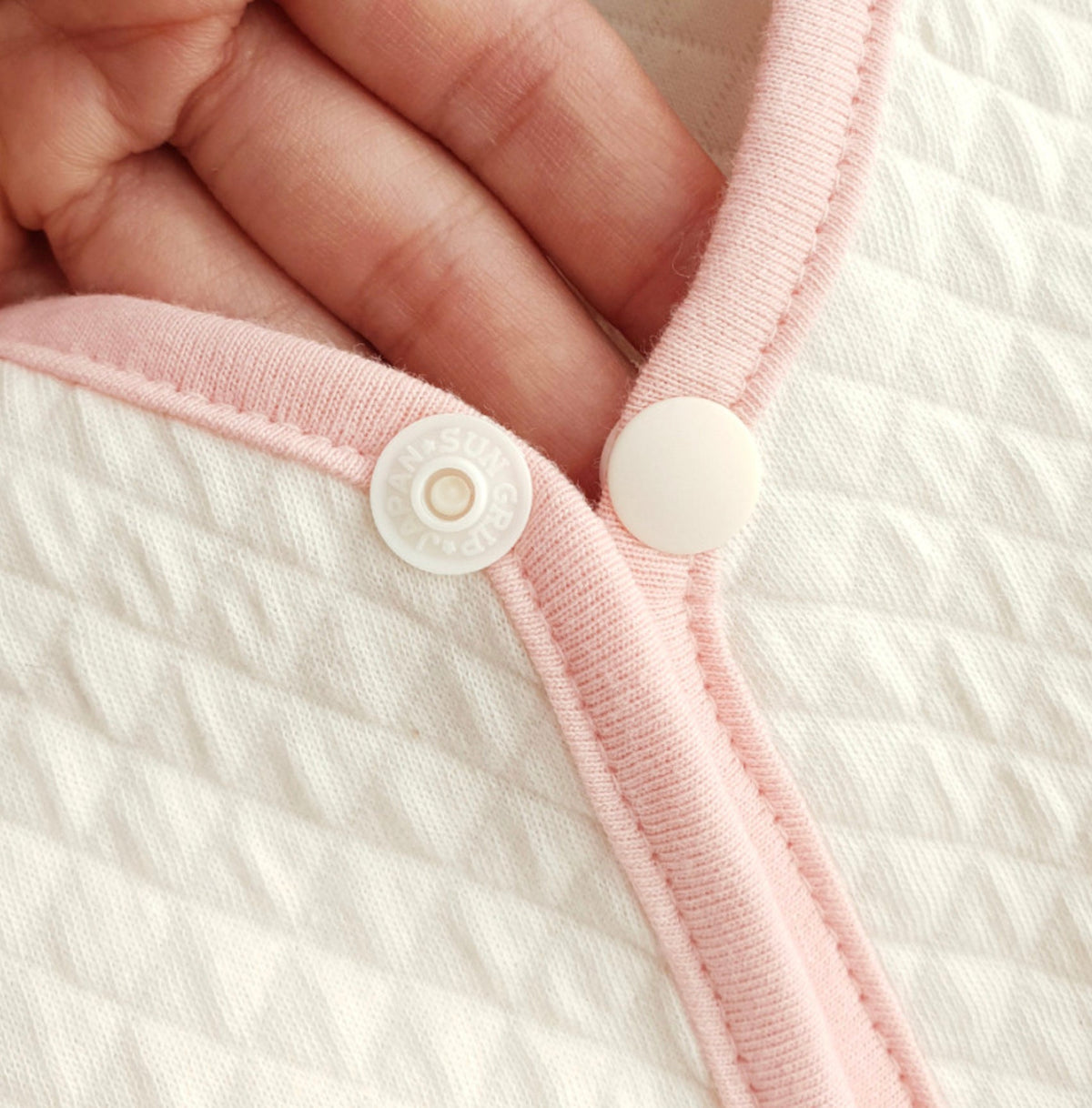 White organic quilted dog vest with pink trim and snap button closure.