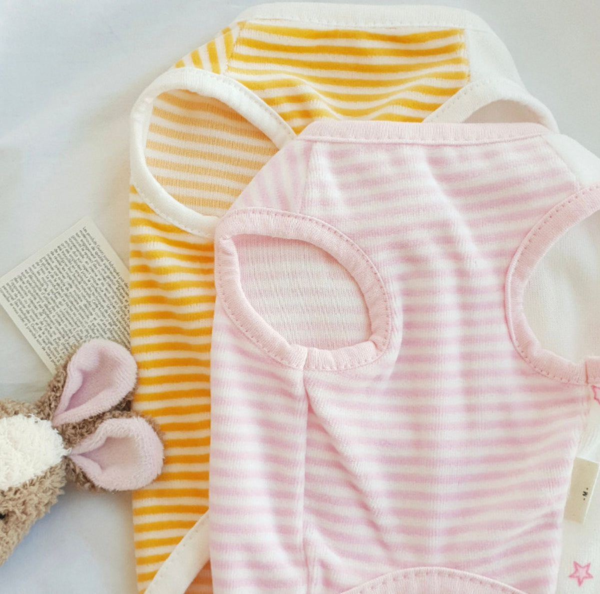 Two striped pet vests, one yellow and white and one pink and white.