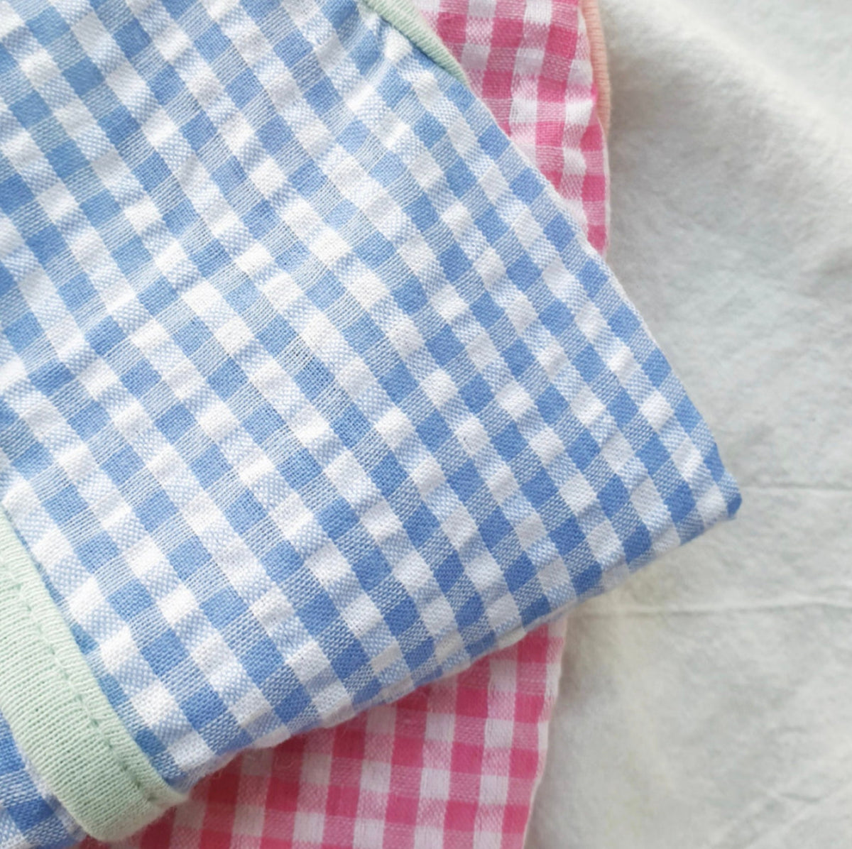 Close-up of NKpup vintage-inspired gingham dog vests in blue and pink check patterns.