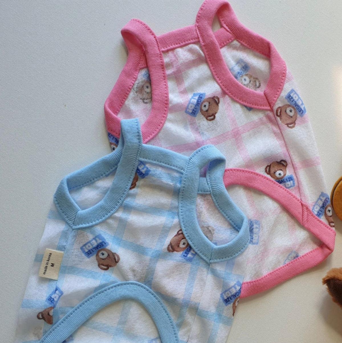 Two teddy bear patterned dog tank tops in pink and blue plaid patterns.