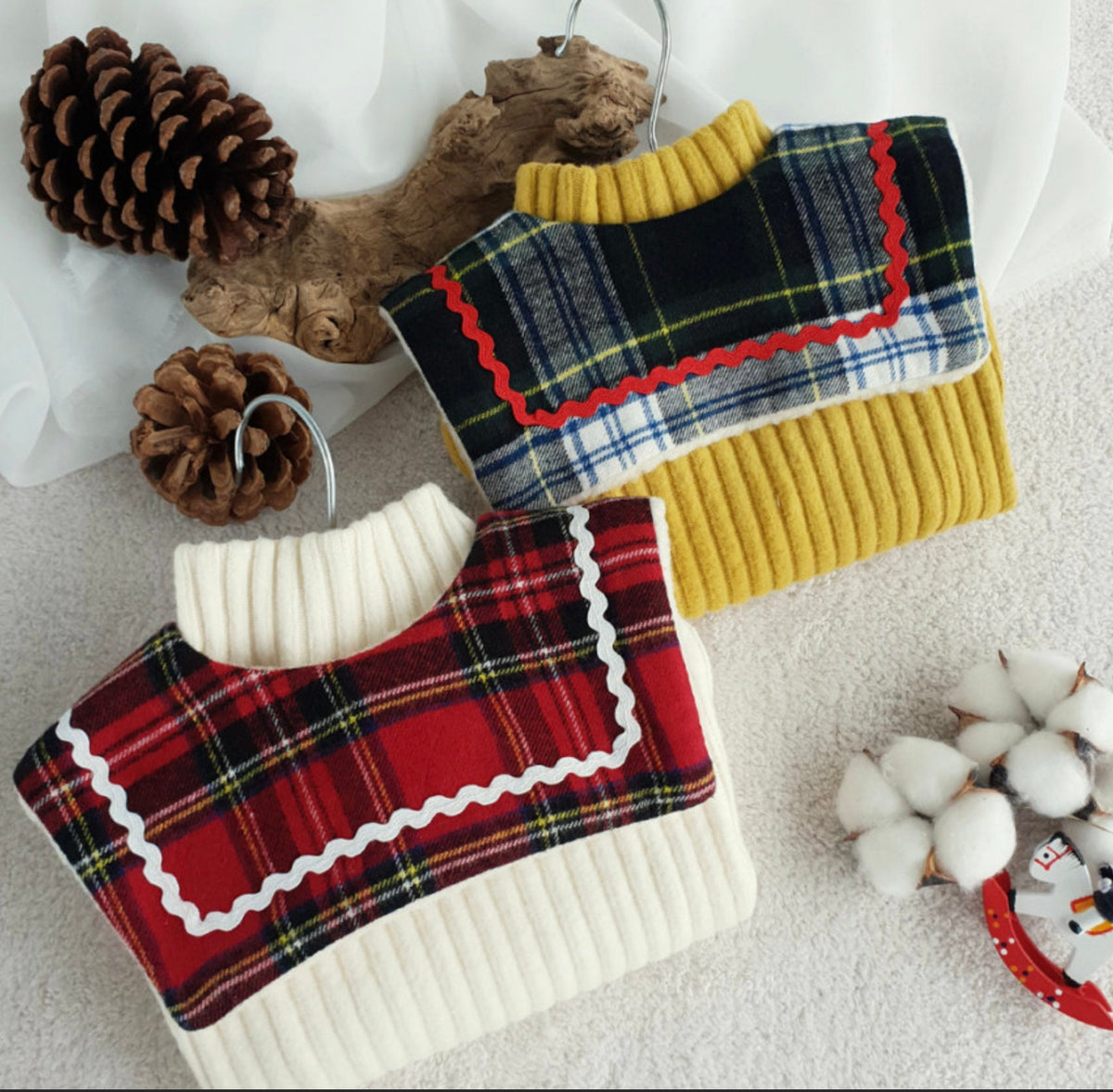 NKpup reversible plaid dog capes in red and blue tartan patterns over ribbed knit sweaters.