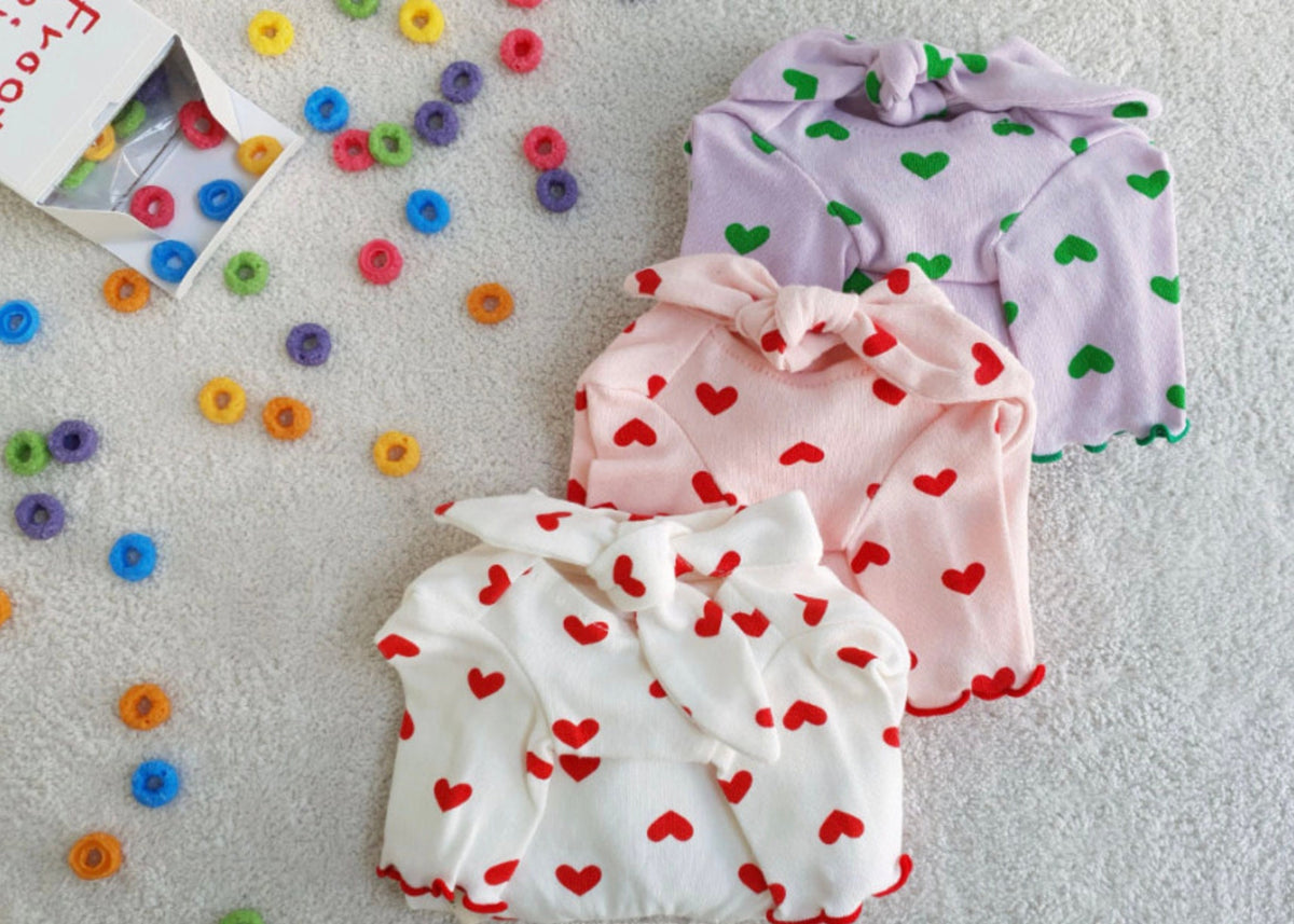 Three NKpup heart tie dog shirts in white, pink, and lavender with colorful heart patterns.