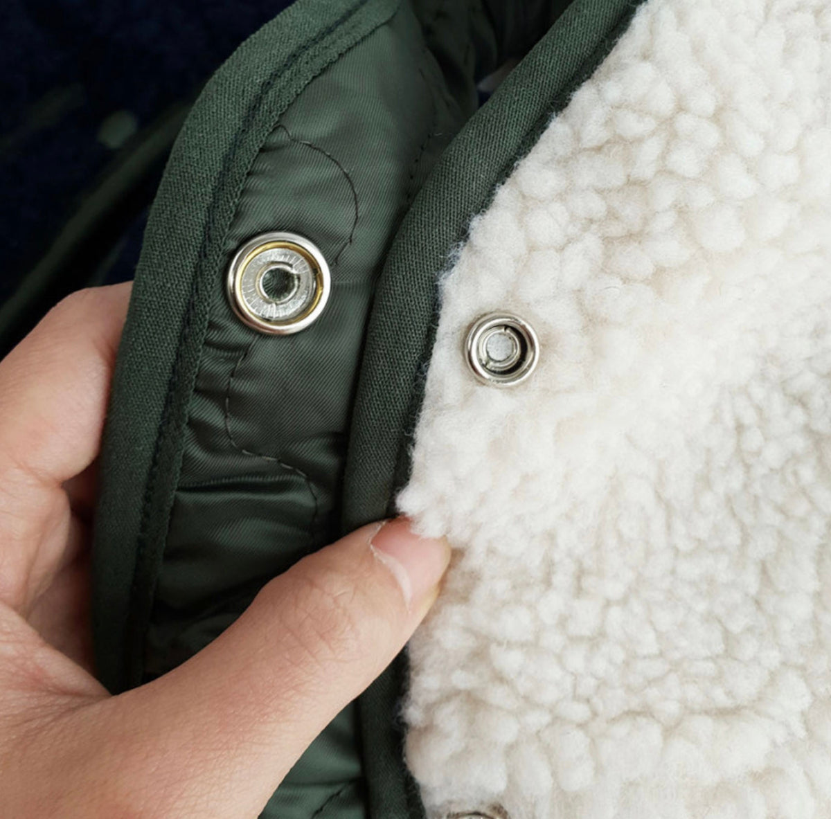 Close-up of the reversible olive green nylon and white sherpa fleece lining of an NKpup dog vest.