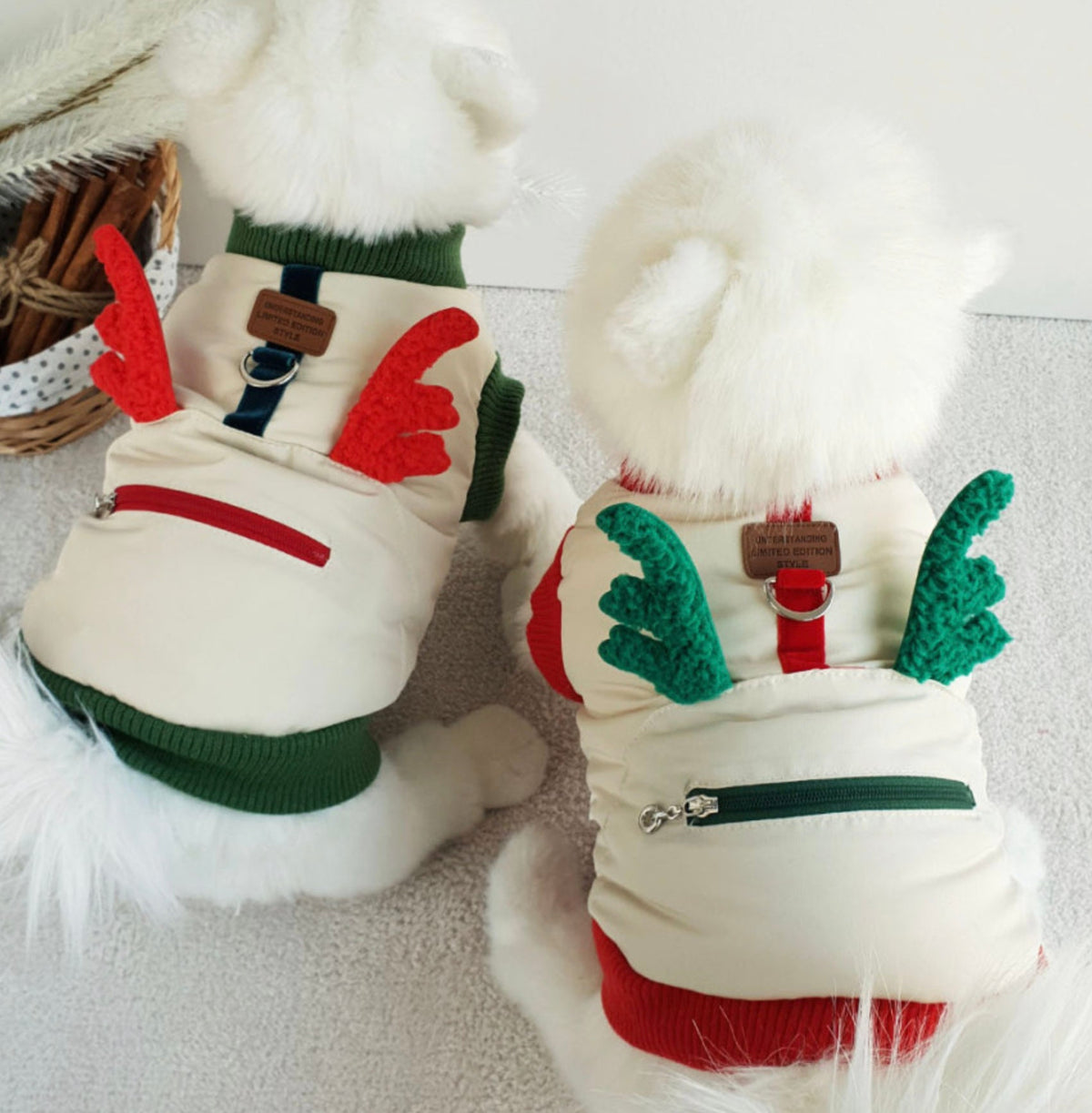 Two white dogs wearing Christmas Rudolph padded dog vests with reindeer antler designs.