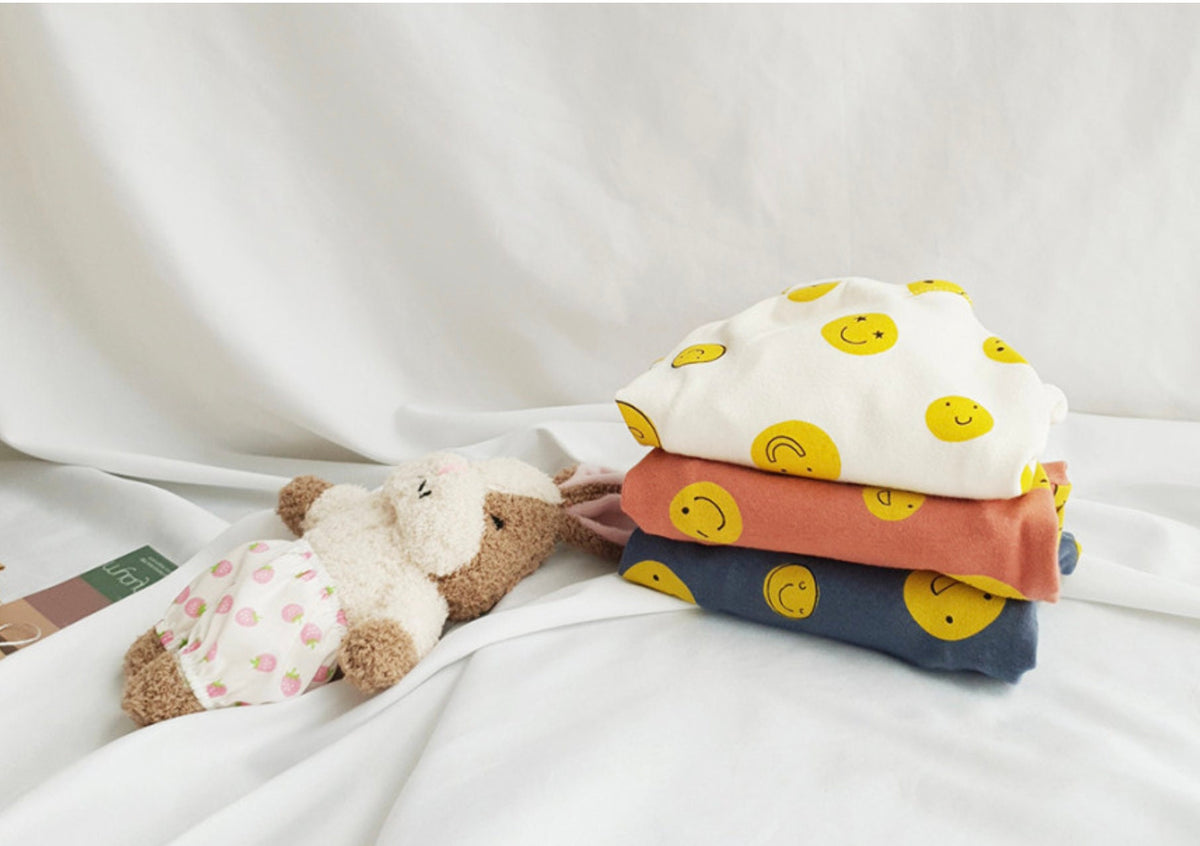 Stack of NKpup Smile Face Dog Overalls in white, terracotta, and navy blue with yellow smiley faces