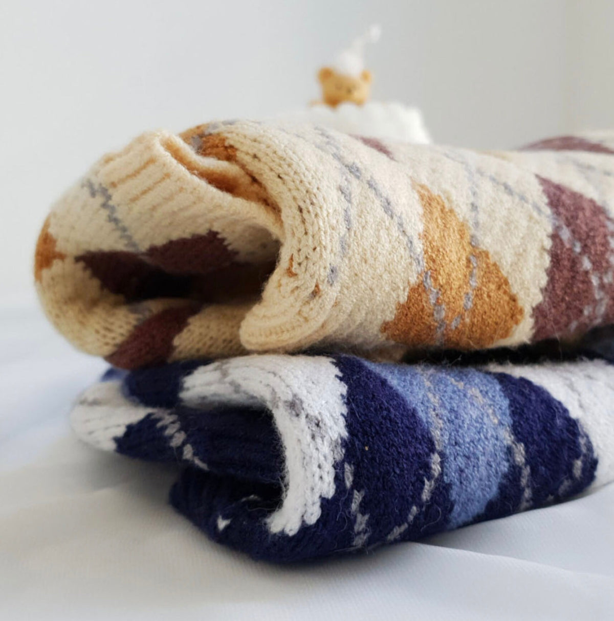 Argyle knit dog sweaters in beige and navy blue patterns.