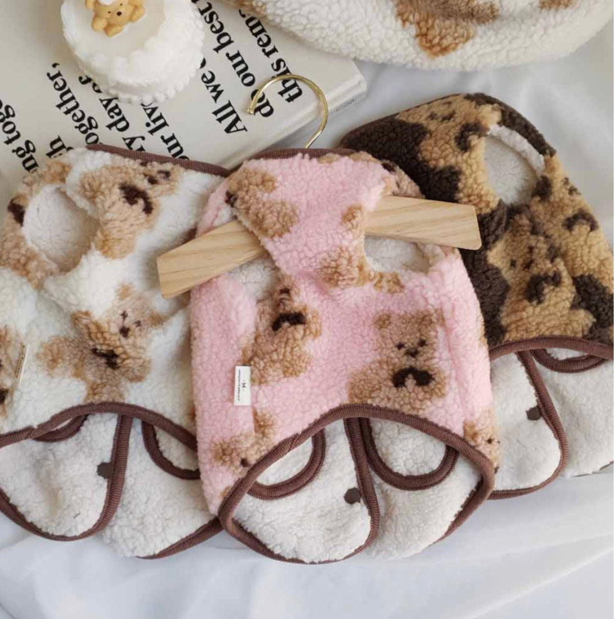 Three reversible bear fleece dog vests in white, pink, and brown colors.