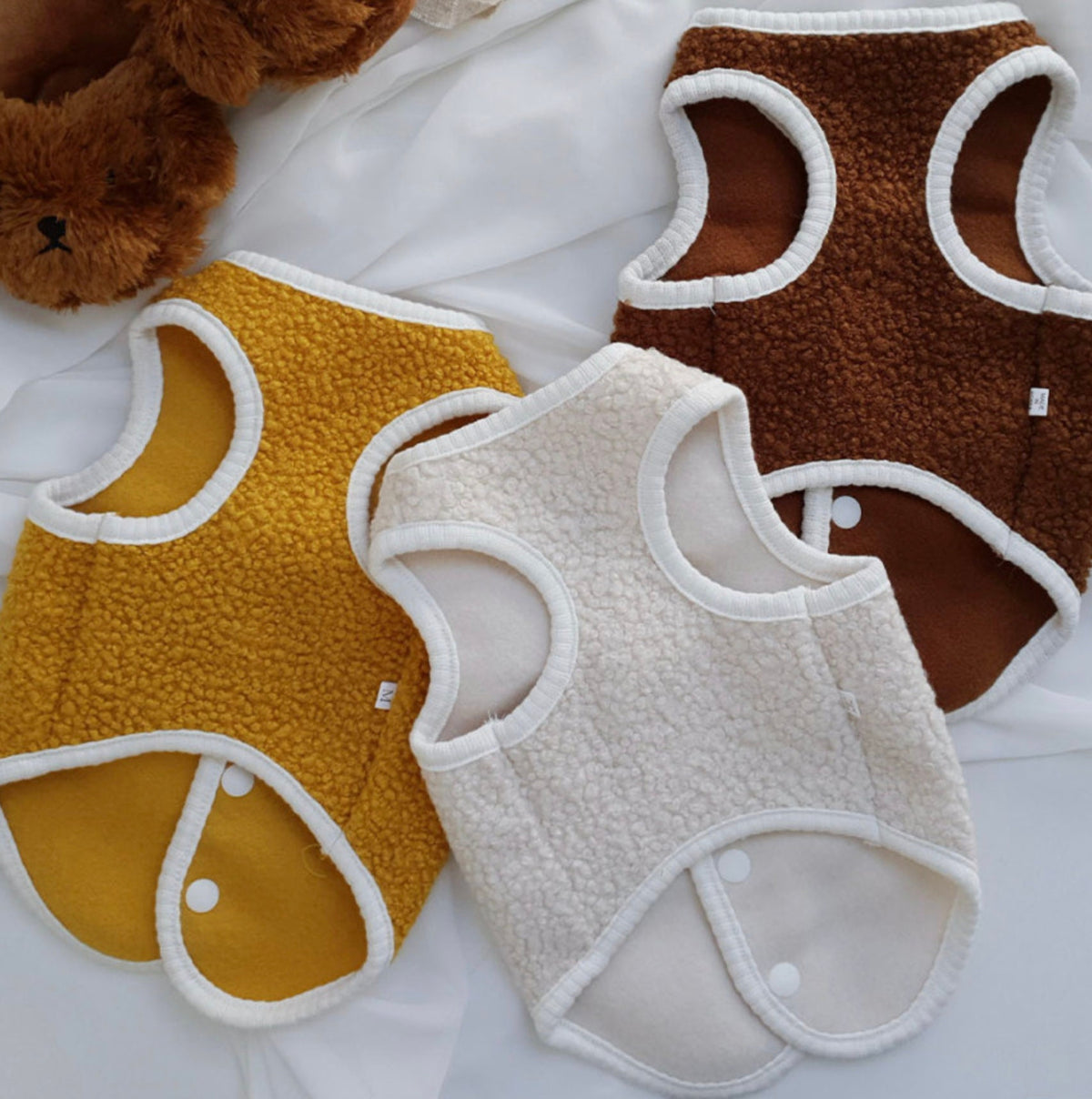 Three bear fleece dog vests in mustard yellow, brown, and cream colors.