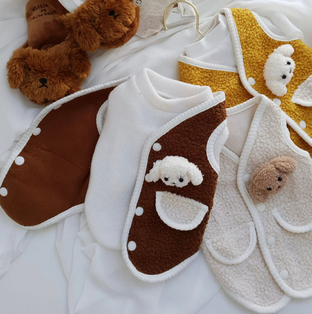 Set of three plush fleece dog vests in brown, white, and mustard yellow with cute animal face appliqués.