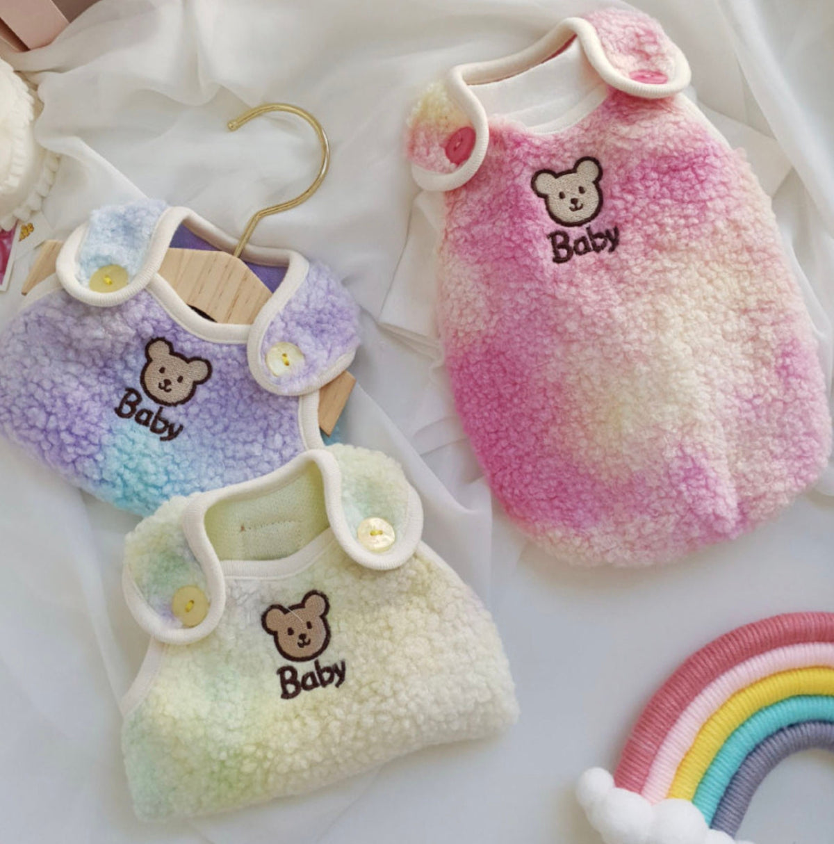 Three Aurora Boa Fleece dog vests in pink, purple, and cream with teddy bear embroidery.