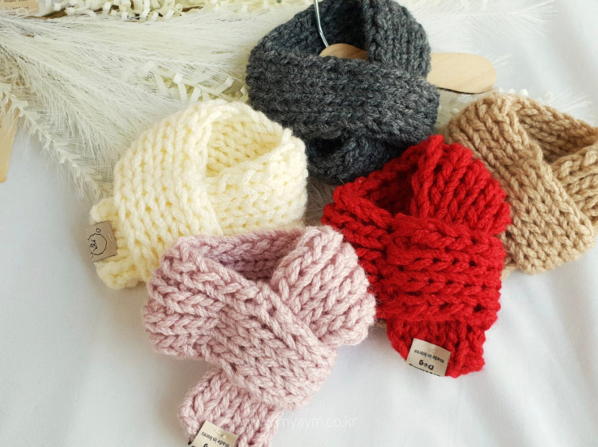 Assorted handmade knit dog scarves in cream, charcoal, tan, red, and pink.
