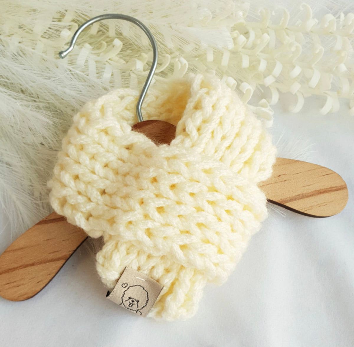 Cream colored handmade knit dog scarf hanging on a wooden hanger
