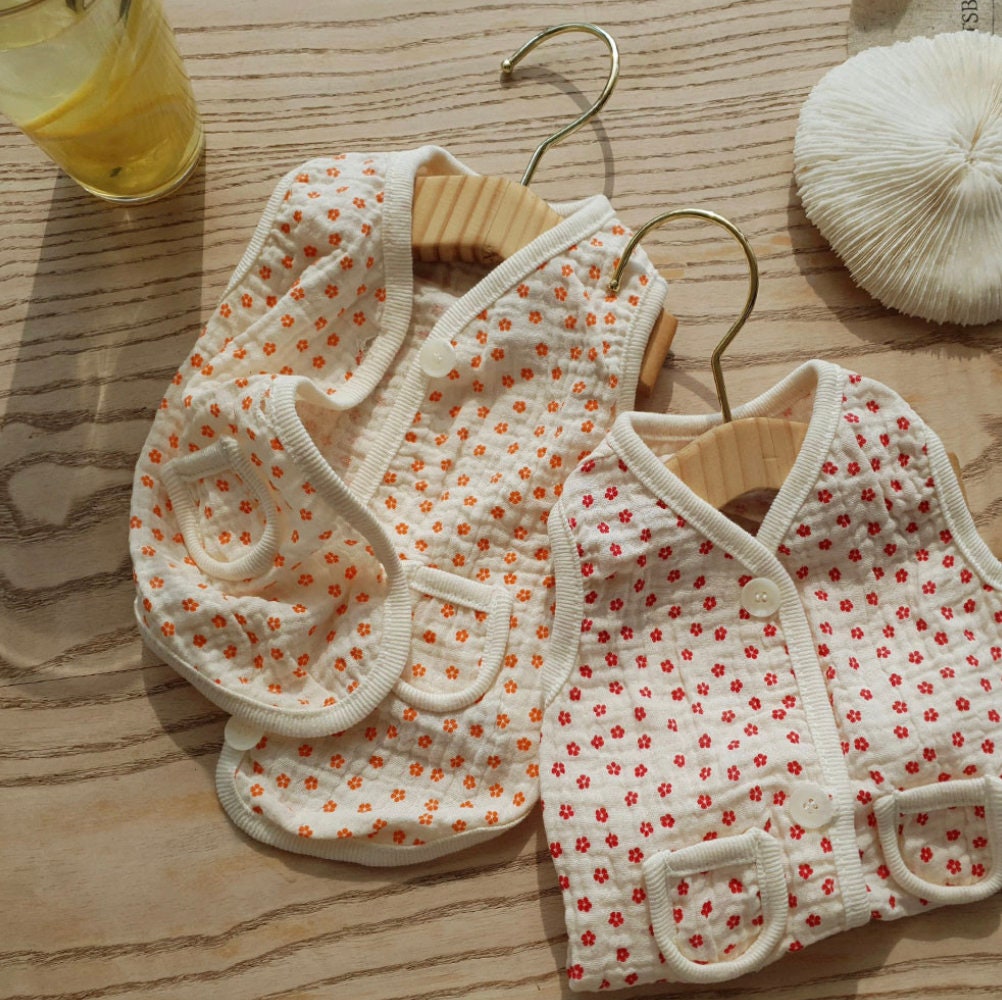 Two crinkle floral dog vests in white with orange and red flower patterns hanging on wooden hangers.