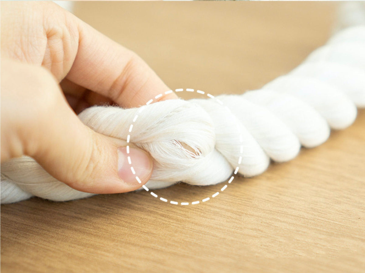 A hand holding a thick white cotton rope dog toy knot.