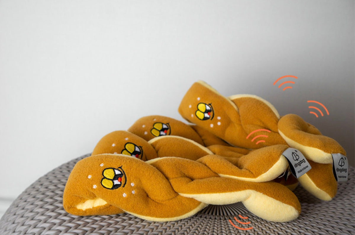 Yellow pretzel-shaped snuffle dog toy with a cute face design.