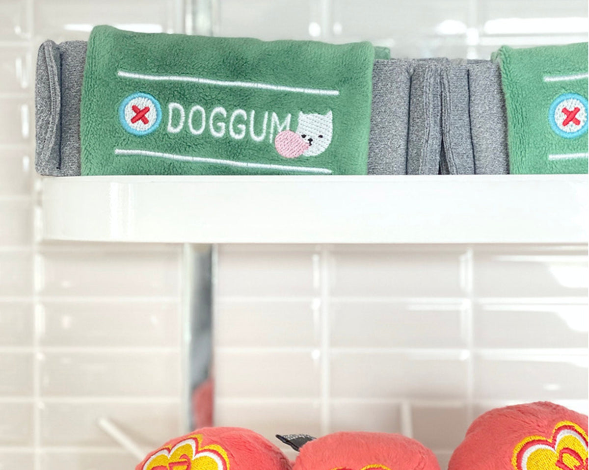 Green and grey folded pet towels with DOGGUM text and cartoon dog embroidery.