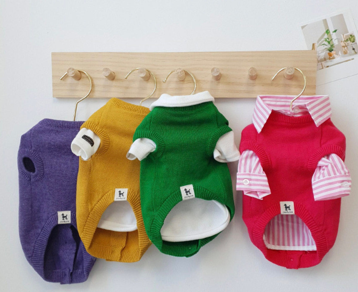 Four colorful NKpup knit dog cardigan vests in purple, yellow, green, and pink hanging on a wooden rack.