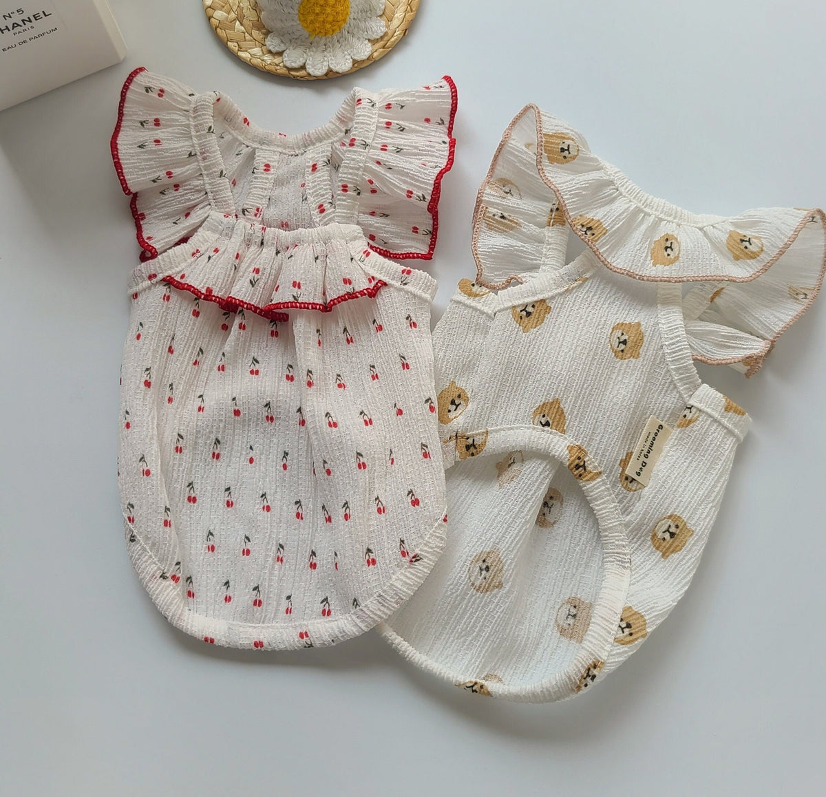 Two NKpup sleeveless dog dresses with ruffled wings; one white with red cherry print and one with bear print.