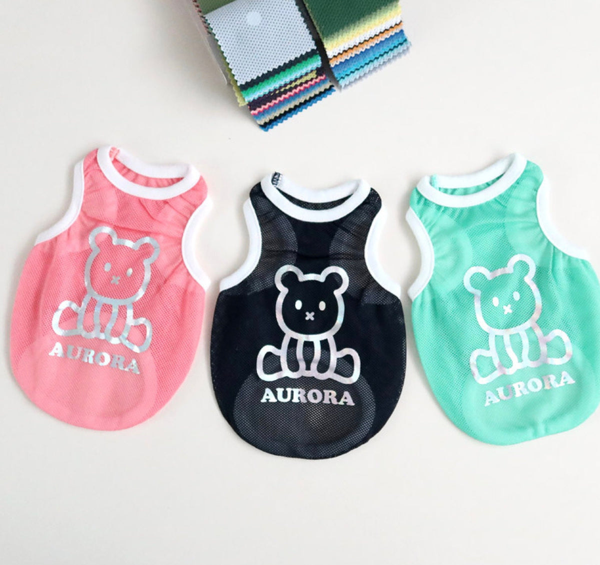 Three Aurora Mesh Sleeveless dog vests in pink, black, and mint green featuring a bear graphic.