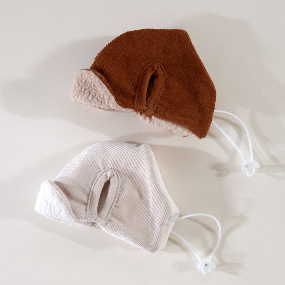 Two corduroy pet bomber hats in brown and cream with soft fleece lining and adjustable chin straps.