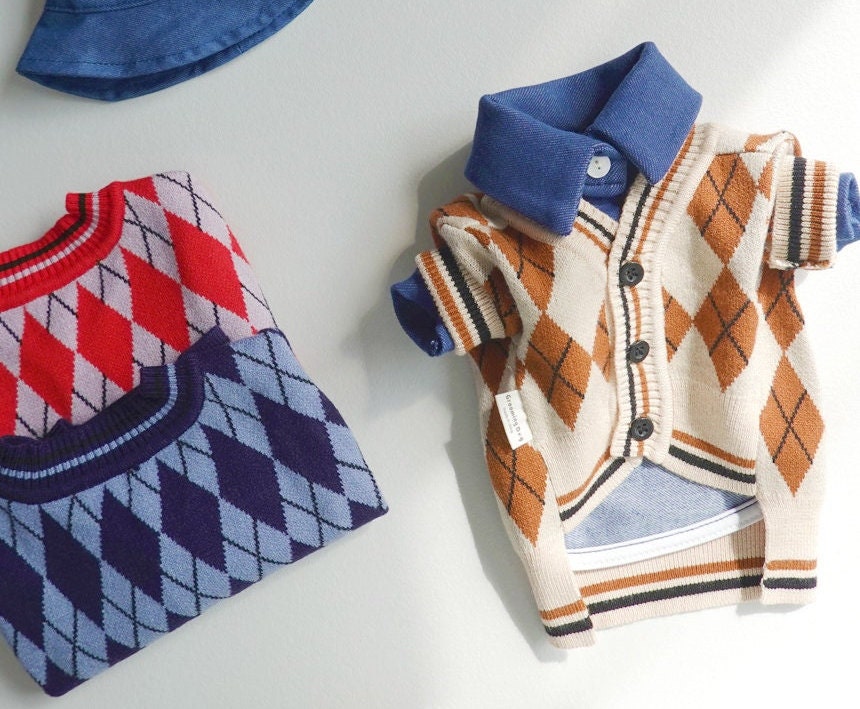 Argyle knit dog cardigan in beige with brown diamond patterns and a blue collared shirt underneath.