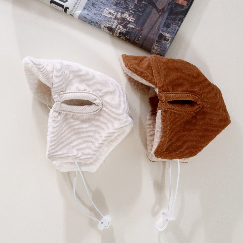 Two corduroy bomber hats for pets in cream and brown colors with fleece lining and chin straps.
