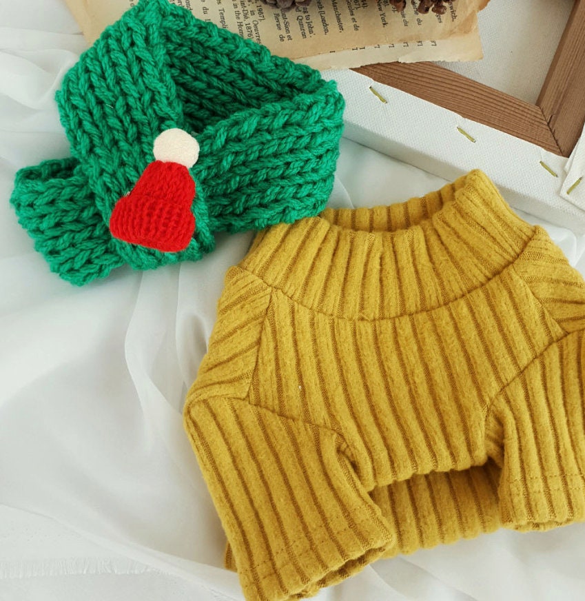 Green handmade knit Christmas dog scarf with a red and white pom-pom and a mustard yellow ribbed dog sweater.