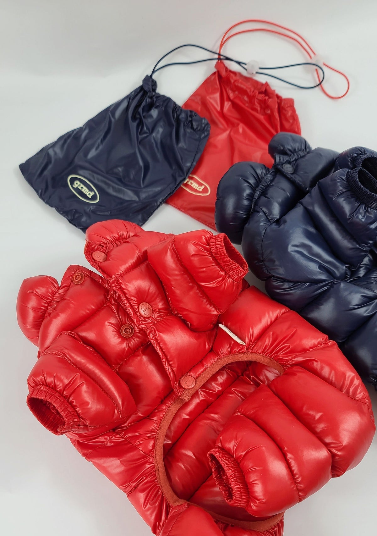 Red and navy blue lightweight padded dog overalls with matching drawstring storage bags.