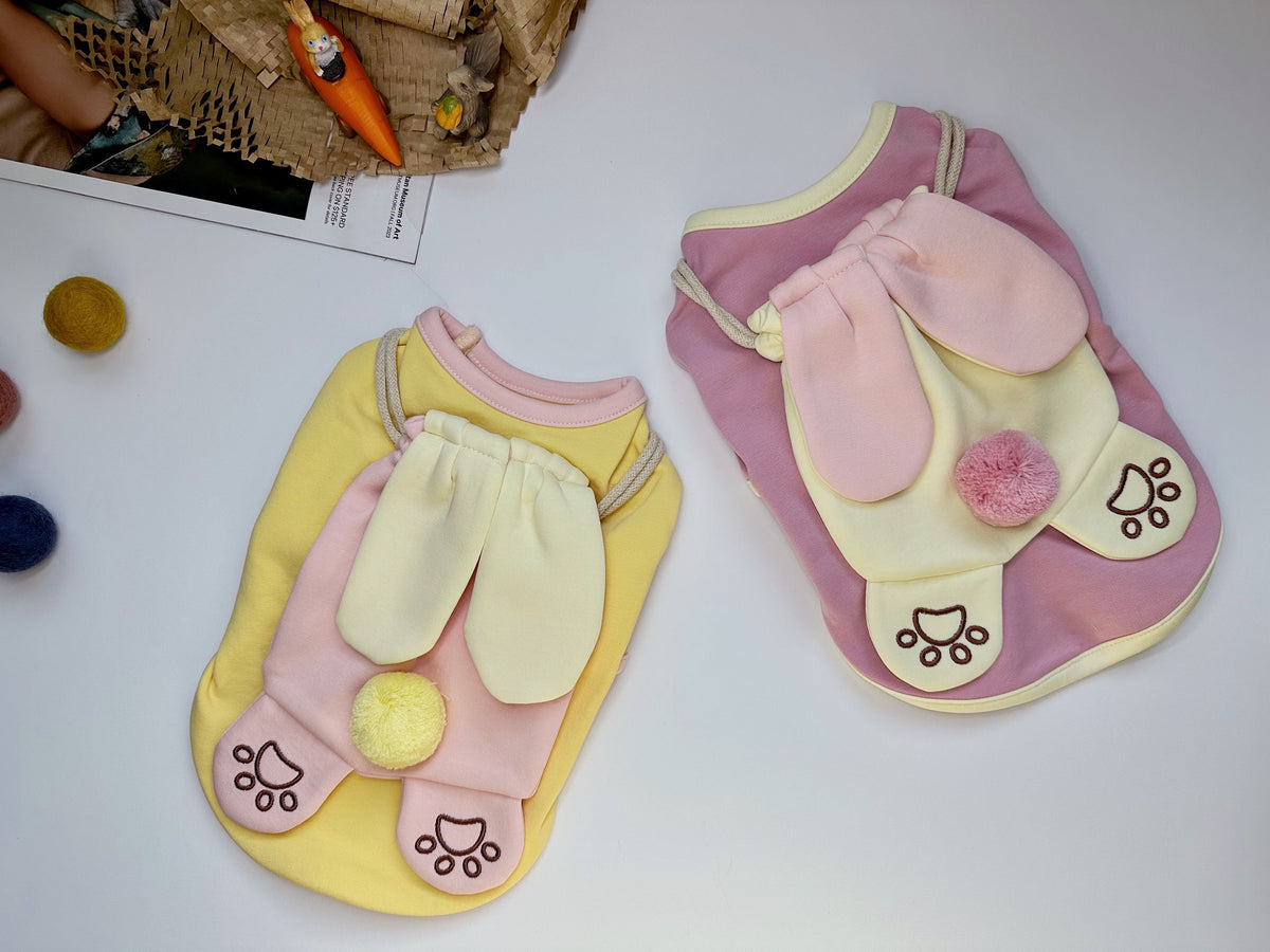 Two NKpup Bunny Bag Dog Shirts in yellow and pink with decorative bunny ears and pom-poms.